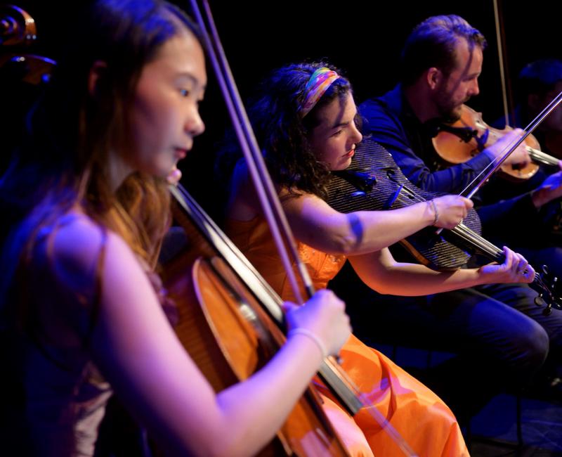 Three musicians sitting side by side playing string instruments
